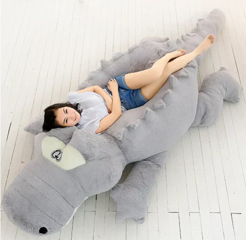 world's largest plushie of a grey crocodile with a woman laying on top